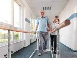 Senior,Patient,And,Physical,Therapist,In,Rehabilitation,Walking,Exercises Physical therapist working with a senior patient in rehabilitation