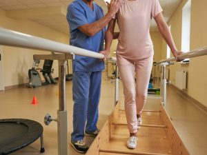 Female,Patient,Uses,Parallel,Bars,To,Walk,In,Rehab,Center Patient using parallel bars during rehabilitation therapy