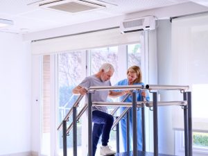 Senior,Man,Using,Parallel,Bars,With,Physiotherapist,Assistance,For,Mobility Physiotherapist assisting a patient during rehabilitation